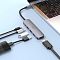 Фото-4 USB-C хаб Hoco HB27 в использовании: подключён к ноутбуку на светло-голубой поверхности, рядом кабели и USB-устройства (флеш-накопитель, переходники); фото показывает типичный сценарий расширения портов.