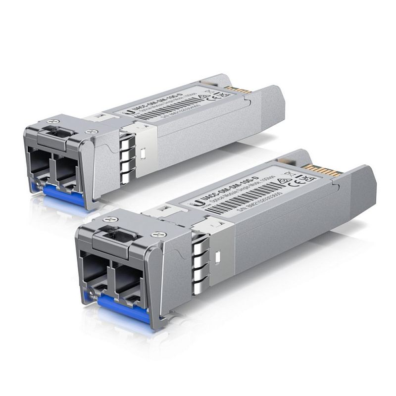 Фото-1 Трансивер Ubiquiti UACC‑OM‑SM‑10G‑D‑2 (комплект), на фото два модуля под углом: спереди установлены синие защитные заглушки оптических гнёзд, на корпусах наклейки с маркировкой и элементы защёлки. Серебристые корпуса с синими заглушками, на белом фоне; помогает распознать комплект SFP‑модулей и состояние разъёмов для подключения оптики.