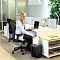 Фото-3 Уничтожитель бумаги Fellowes Powershred LX41 в офисном интерьере у тумбы: устройство стоит на полу, человек вставляет лист в верхний слот, видна передняя часть с окном корзины; контекст использования важен для понимания высоты и удобства подачи бумаги на странице товара.