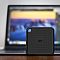 Фото-11 Внешний SSD Silicon Power PC60 2TB на фоне ноутбука, фронтальный вид: чёрный корпус с логотипом SP и отверстием под карабин в левом верхнем углу; помогает узнать лицевую сторону модели.