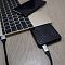 Фото-28 Внешний SSD Silicon Power PC60 2TB рядом с ноутбуком и смартфоном, вид сверху под углом: чёрный корпус с подключённым кабелем USB‑C и отверстием под карабин; помогает увидеть форму и подключение.